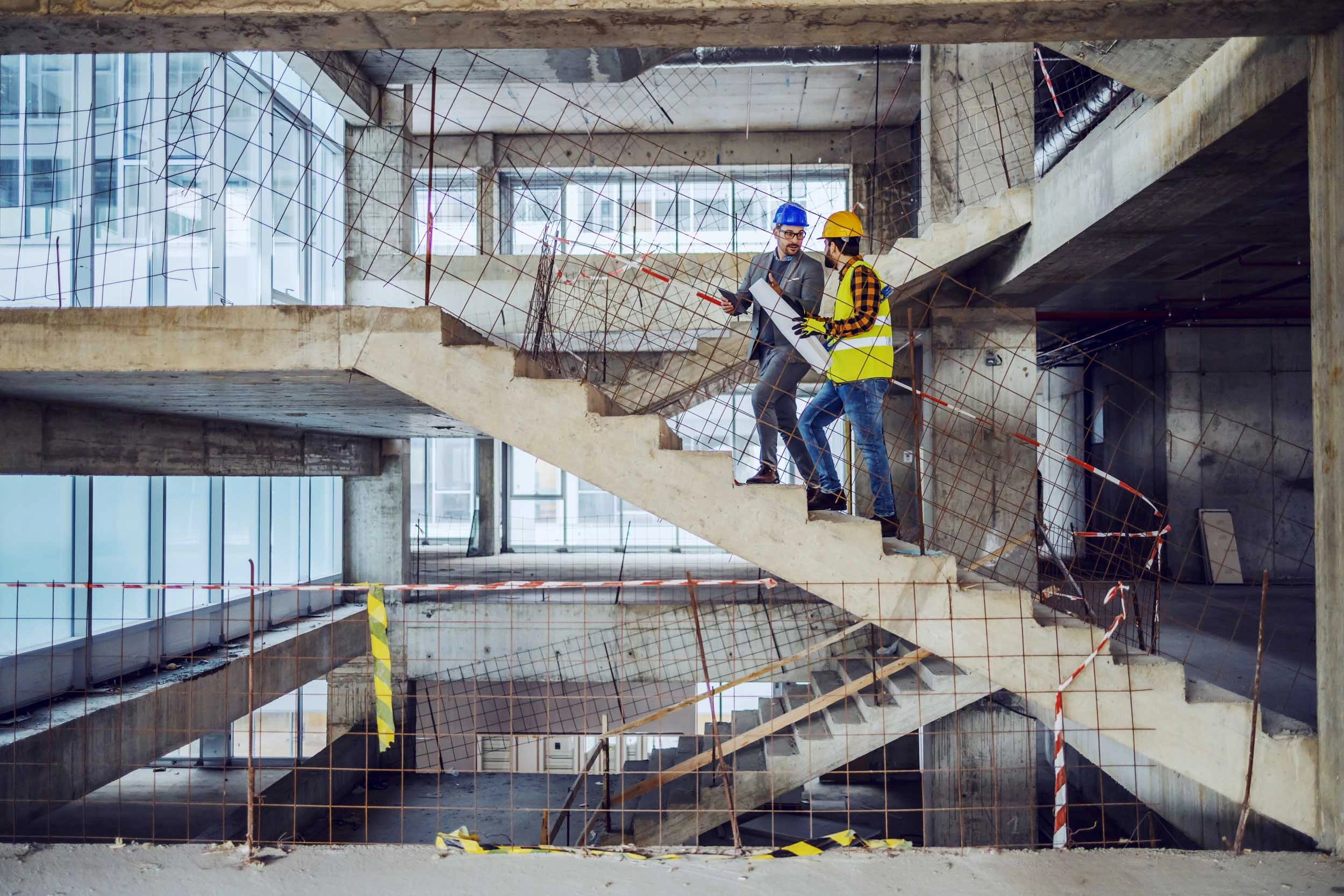 Senior construction manager or director climbing stairs on an ongoing construction site talking to a site manager holding plans
