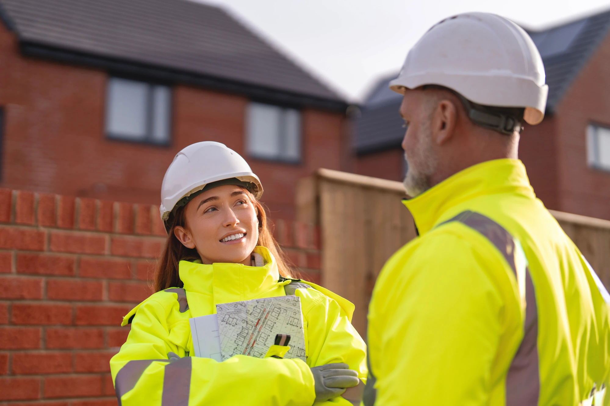 Site supervisor and young construction worker on a new build site talking and smiling wearing PPE