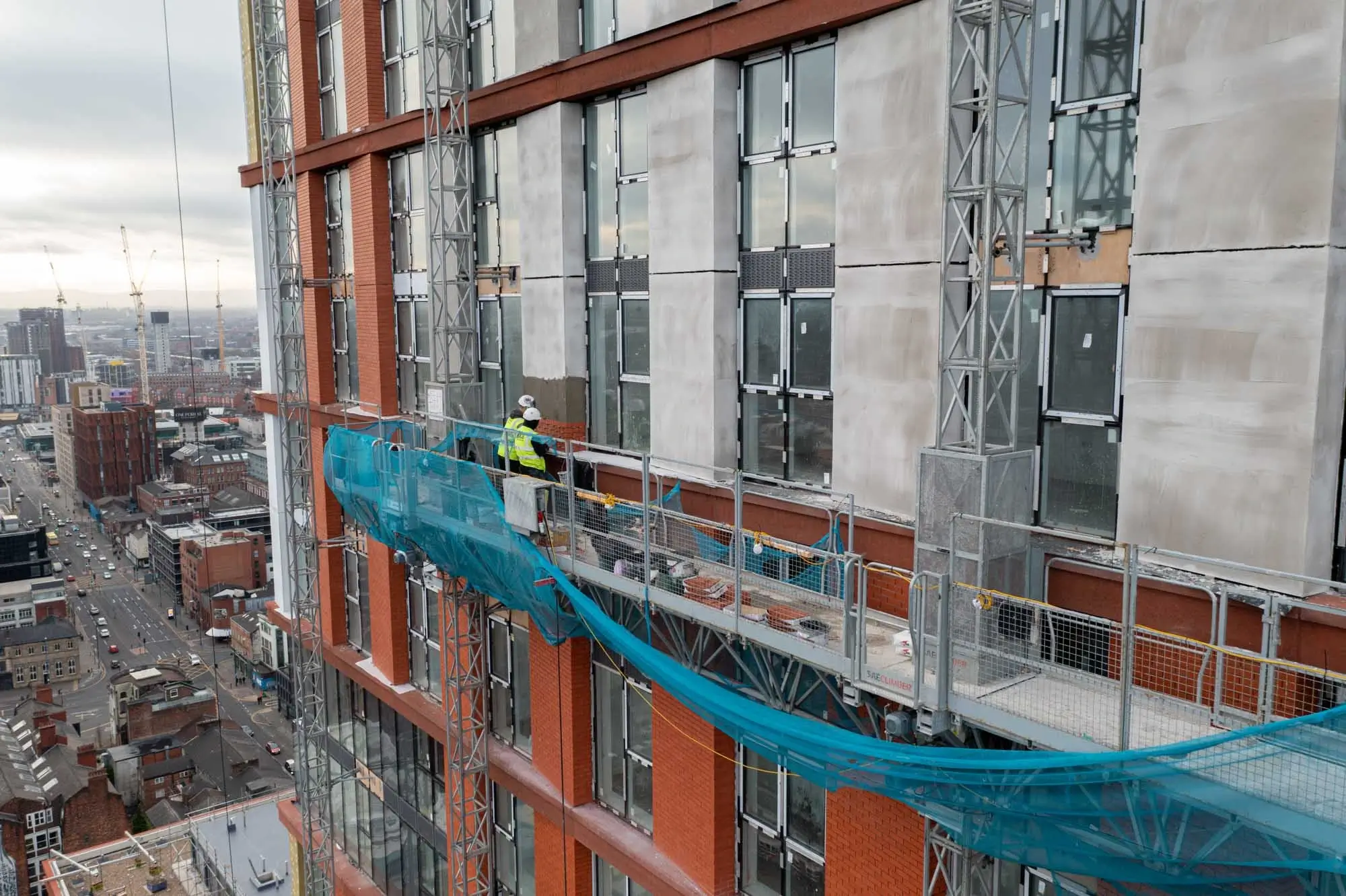 Construction workers working on tower block doing external wall rendering aerial photo